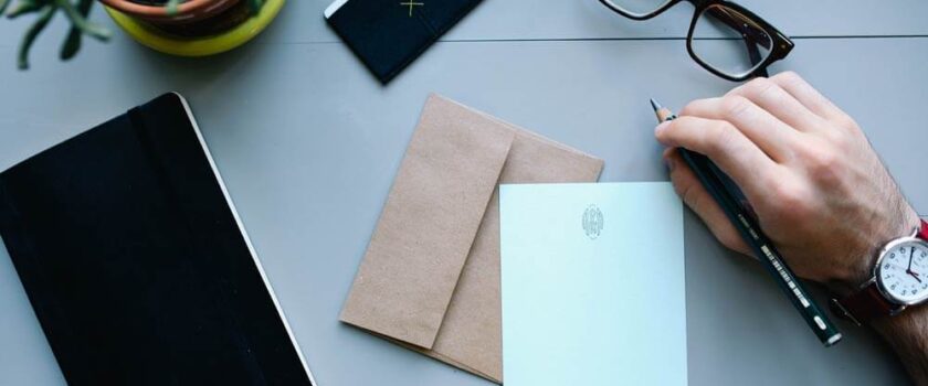 A person writing on paper next to an open envelope.