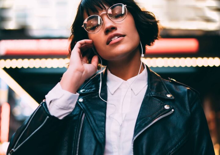 A woman in glasses and leather jacket talking on the phone.