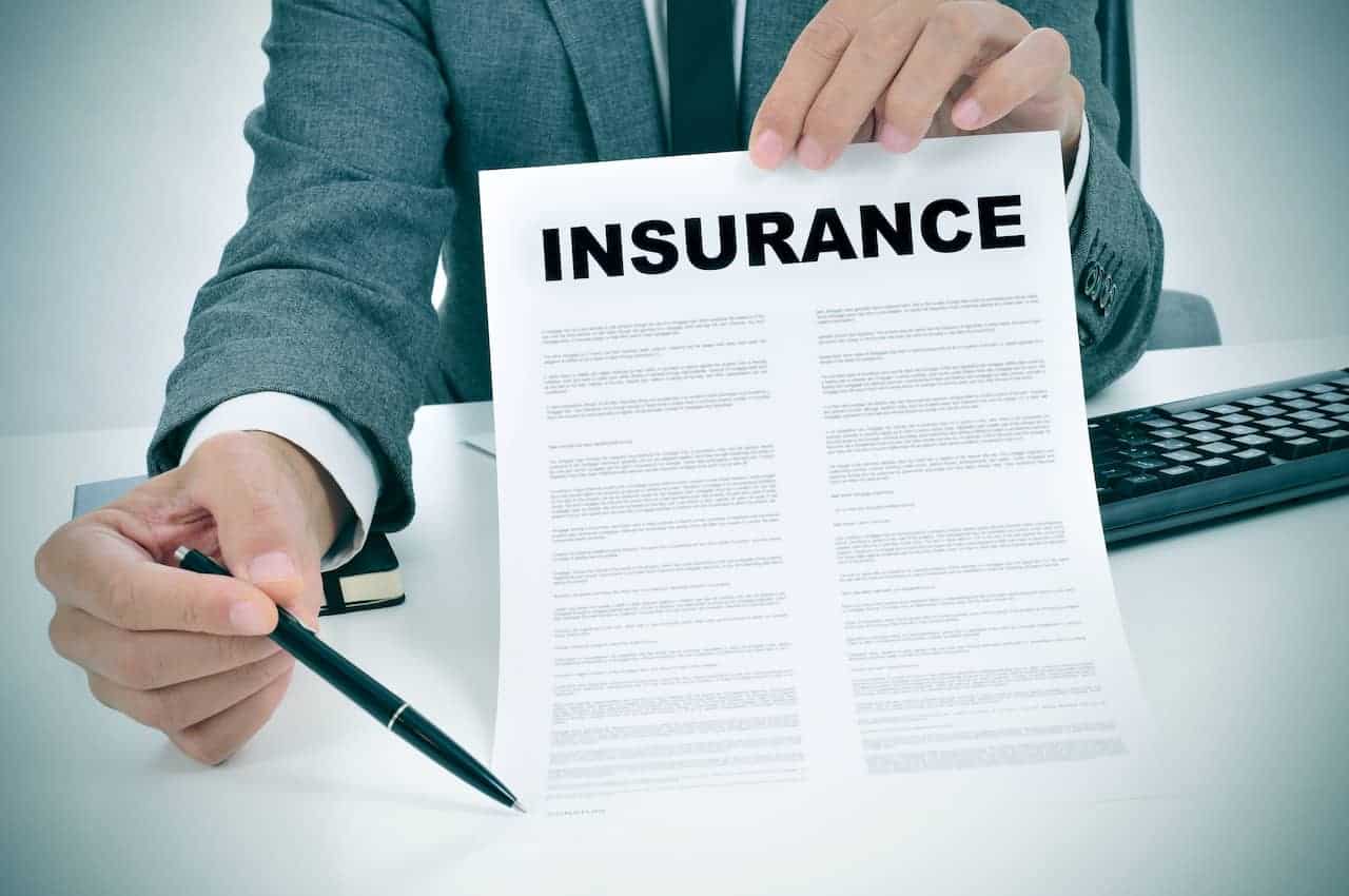 A person is holding an insurance document and pen.